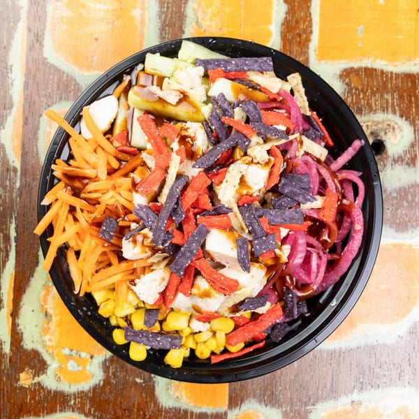 Overhead view of a colorful salad with chicken, corn, carrots, pickled onions, and tortilla strips.
