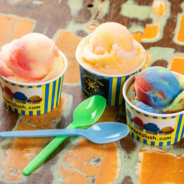Three cups of Sunset Slush Italian ice in various flavors and colors with two plastic spoons.