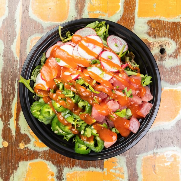 A vibrant poke bowl with tuna, radishes, jalapeños, and a spicy orange sauce on a rustic wooden table.