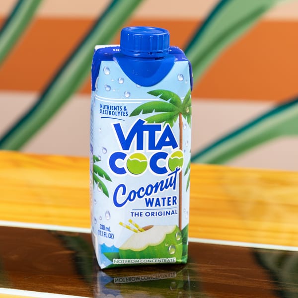 A Vita Coco coconut water carton with a blue cap sits on a wooden surface.