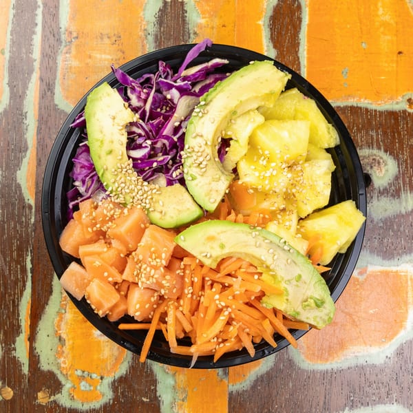 Colorful poke bowl with salmon, avocado, pineapple, red cabbage, and shredded carrots.