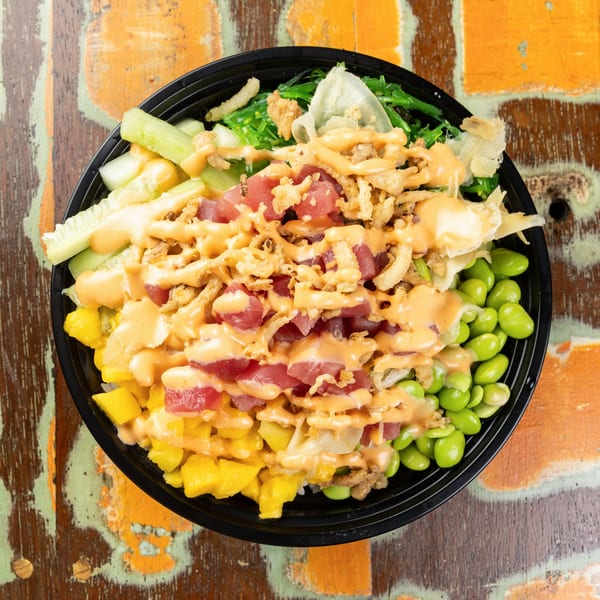 Top-down view of a poke bowl with tuna, mango, edamame, seaweed, and sauce.