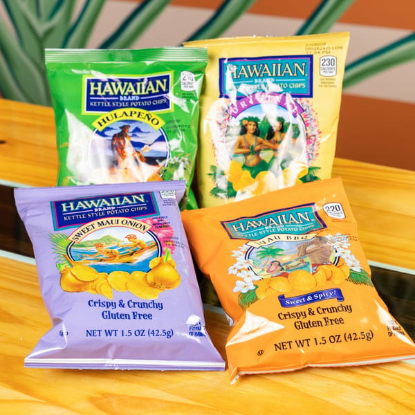 Four bags of Hawaiian Brand Kettle Style Potato Chips in various flavors on a wooden surface.