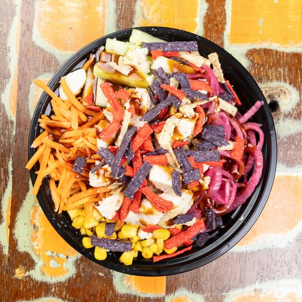 Overhead view of a colorful salad bowl with chicken, corn, carrots, pickled onions, and tortilla strips.